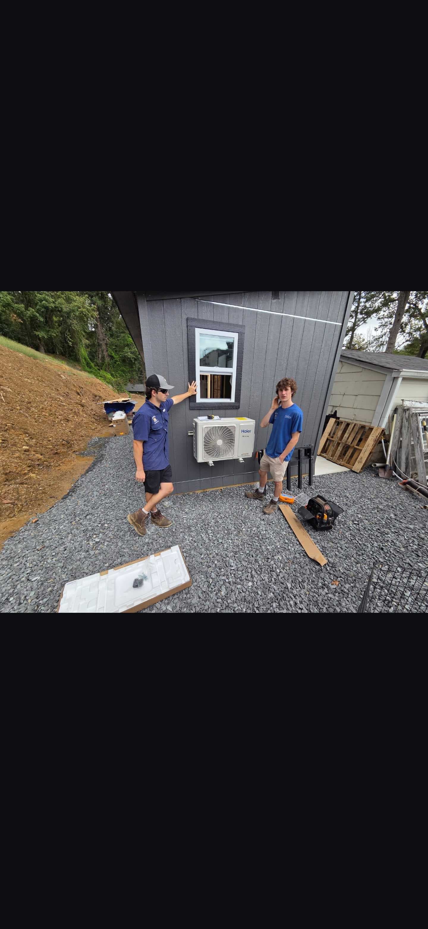 Prince crew members beside a wall-mounted outdoor mini-split unit.
